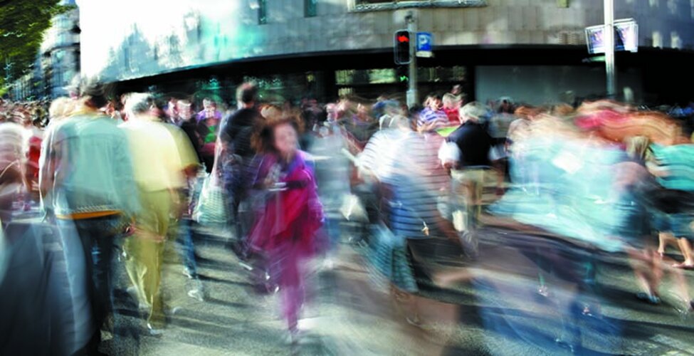 En suddig bild av människor som går på en trafikerad gata i storstadsmiljö.