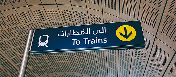 Vägskylt som visar vägen till tågen både på engelska och modern arabiska