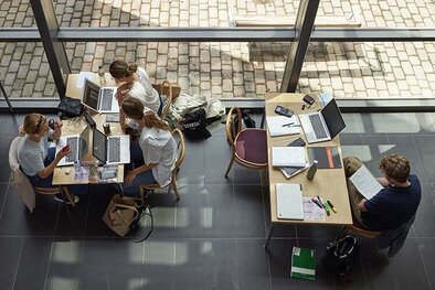 Fyra studenter pluggar vid två olika bord. Bilden är tagen ur ett fågelperspektiv. 