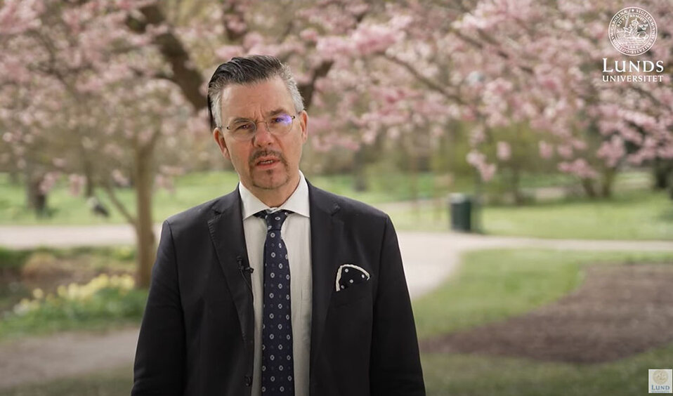 Vice-chancellor Erik Renström is standing in a park, in front of blossoming cherry trees. He is wearing a suit and tie.