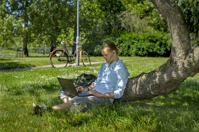  En student sitter på gräsmatten med sin dator